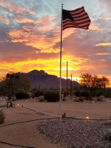 Taxidermist American flag in Arizona. Planted in the ground with a beautiful sunset with orange and yellow, glowing below a splash of blue sky.